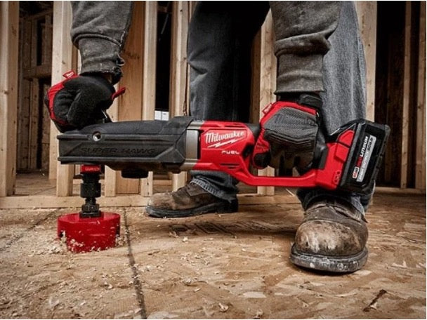 A person wearing work gloves uses the red Milwaukee® oscillating tool to undercut a wooden door frame near the floor