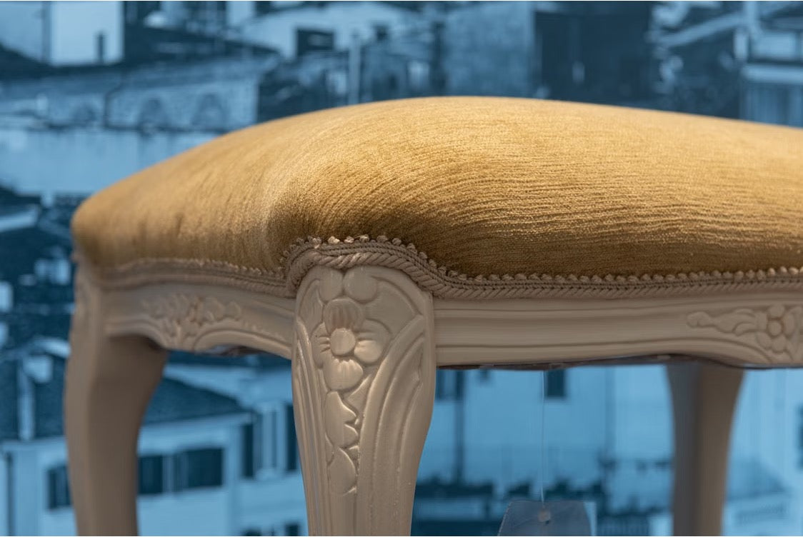 A vintage stool with beige upholstery against a cityscape backdrop