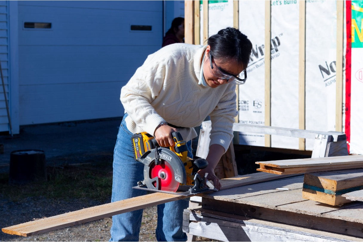 Woman cutting a board on a workbench with a cordless circular saw