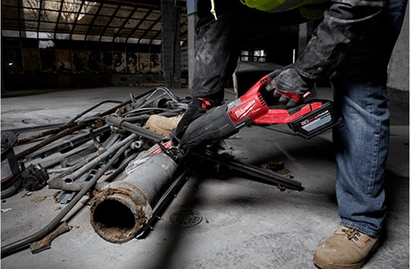 Worker in gloves using a Milwaukee M18 reciprocating saw to cut a metal pipe on a demolition site