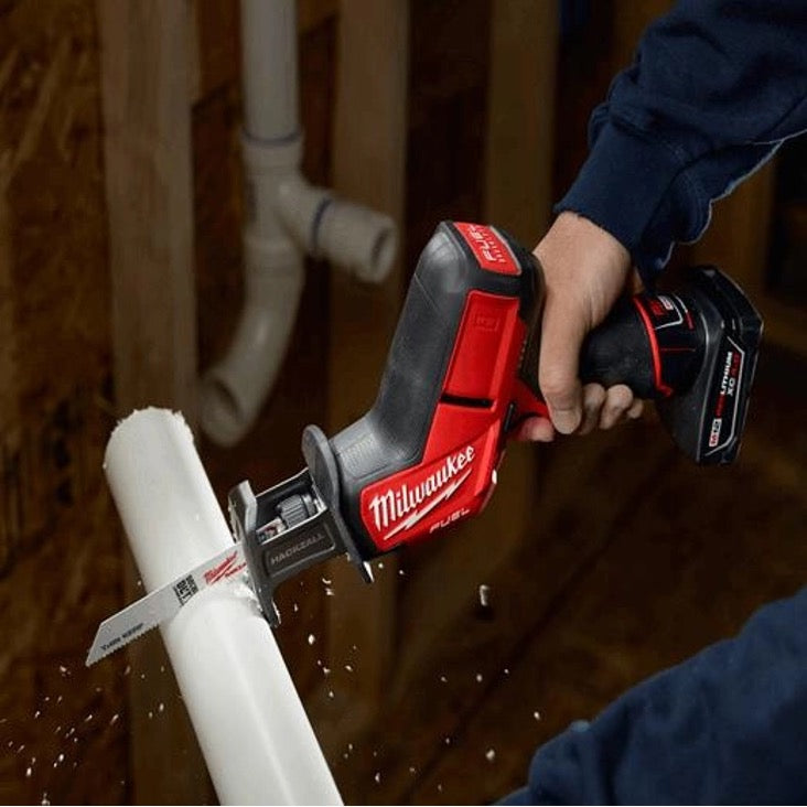 Worker using Milwaukee HACKZALL to cut through white PVC pipe overhead